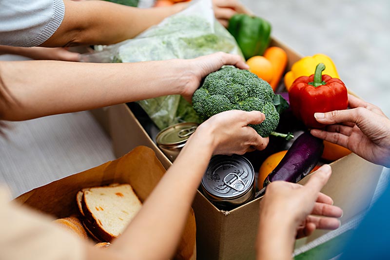 Close up photo of hands putting healthy food into a cardboard box at a food pantry.