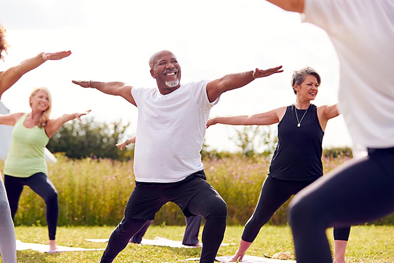 A group of mature adults does yoga outdoors in a park.